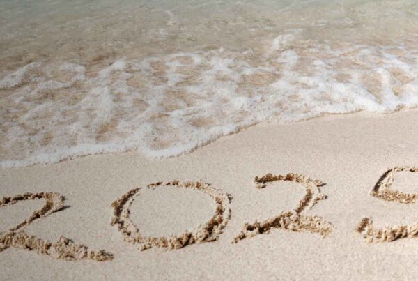 The number 2025 is written in the sand on a beach, with gentle waves approaching the shoreline in the background—perfect for daydreams of travel and airport parking adventures.