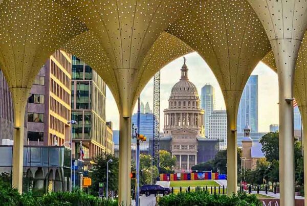 View of the Texas State Capitol framed by modern, golden arches with perforated patterns—an inviting spot for a Family Spring Break in Austin, Texas, surrounded by city buildings and lush greenery.
