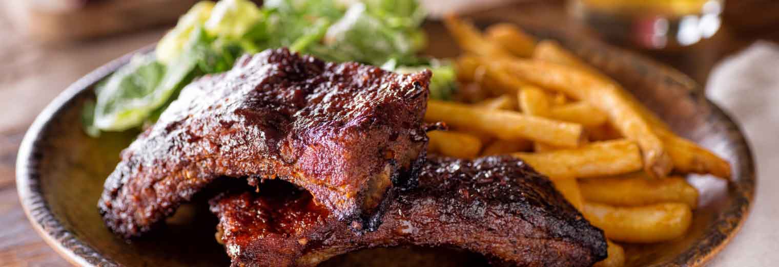 A plate of barbecued ribs with a glazed, crispy exterior, served with golden French fries and a side of green salad—perfect for exploring Great Cities for Your Favorite Foods.