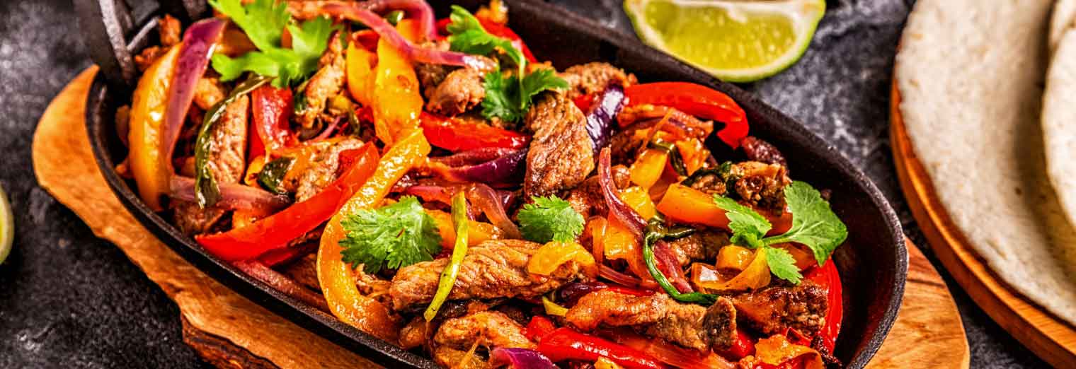 A sizzling skillet of chicken fajitas with colorful bell peppers, onions, and fresh cilantro, served on a wooden tray—just like youd find in the great cities for your favorite foods—complete with lime wedges and warm tortillas nearby.