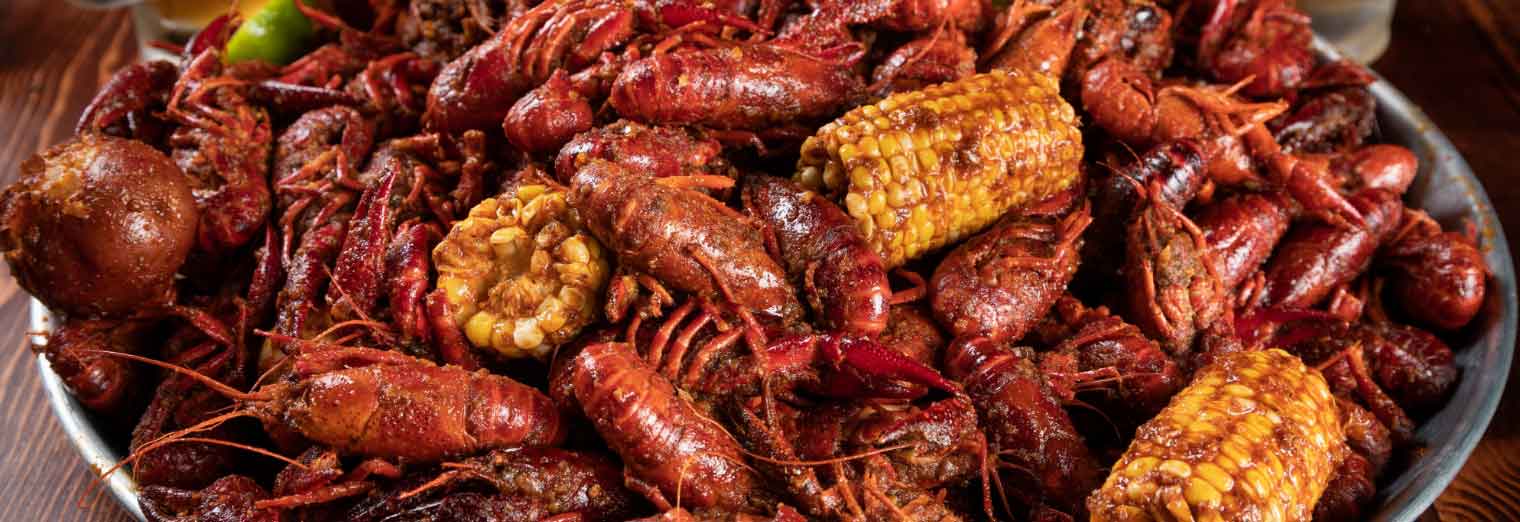 A large platter filled with seasoned boiled crawfish, corn on the cob pieces, and a potato, all coated in spices—a classic feast found in Great Cities for Your Favorite Foods.