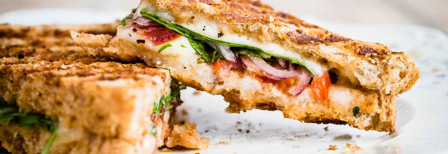 Two halves of a grilled sandwich filled with melted cheese, spinach, sliced tomatoes, and red onions are stacked on a plate—just the kind of bite you’d find exploring Great Cities for Your Favorite Foods.