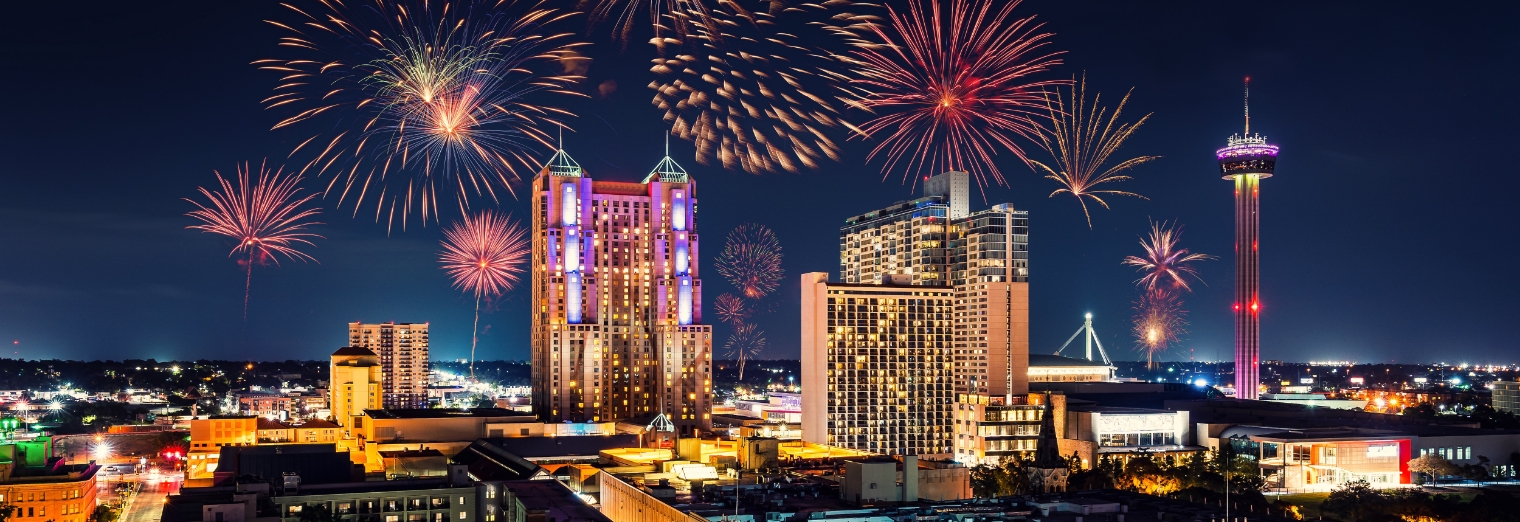 Colorful fireworks light up the night sky above a city skyline with tall buildings and a lit observation tower, creating a festive atmosphere near Joe's Airport Parking.