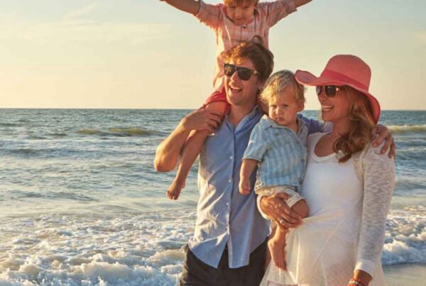 A family of four walks along the beach at sunset, their laughter blending with the sound of waves. Dressed in light, casual clothing, they reminisce about their trip after using Joe's Airport Parking for a smooth start to their vacation.