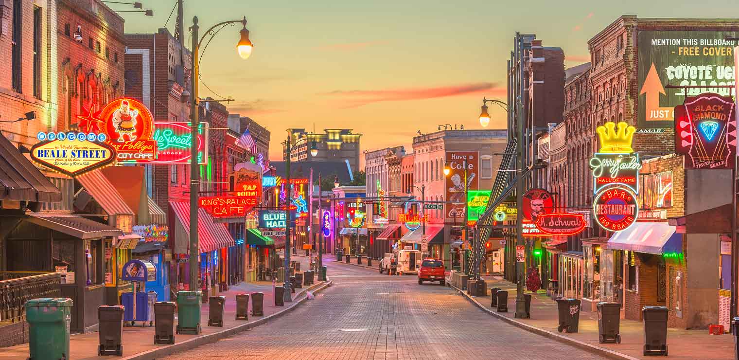 A vibrant city street at dusk, lined with bars, restaurants, and colorful neon signs—including blues and jazz clubs—glows against the evening sky. A sign for Joe's Airport Parking adds a local touch to the mostly empty scene.
